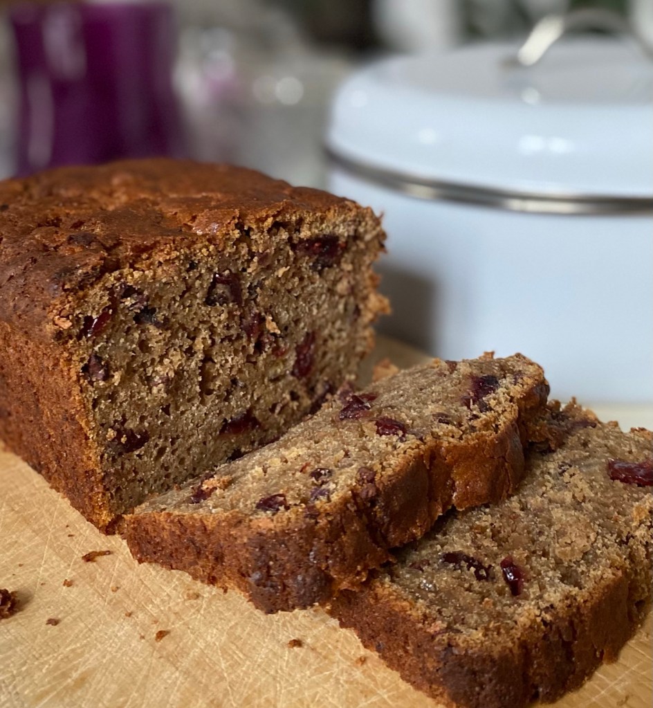 Healthy banana bread loaf with two cut slices on a board made with sourdough starter discard, cranberries and cacao nibs