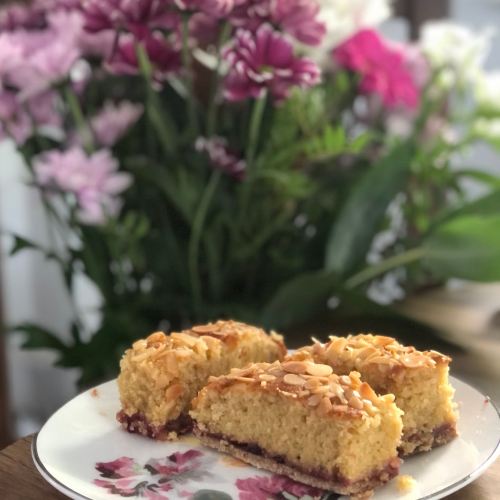 Three damson bakewell tart slices on a plate with flowers in the background